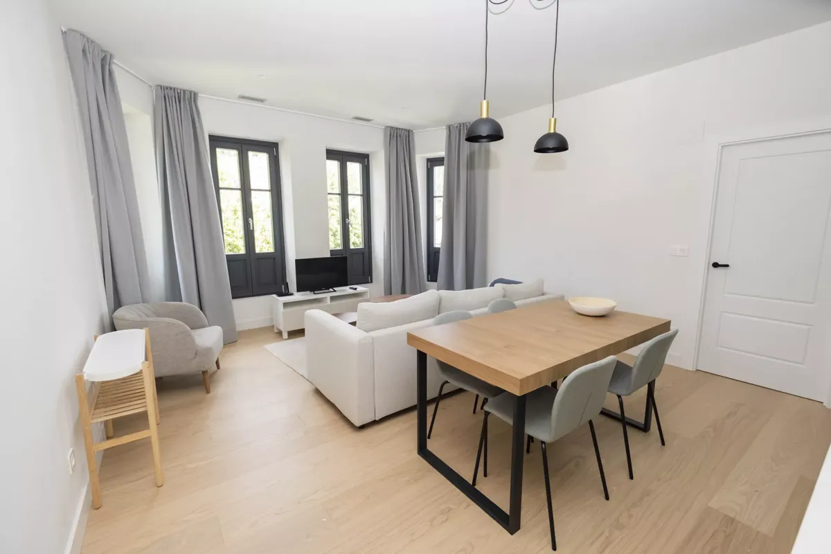 Mesa con sillas, juego de sofá, TV y ventanas con cortinas