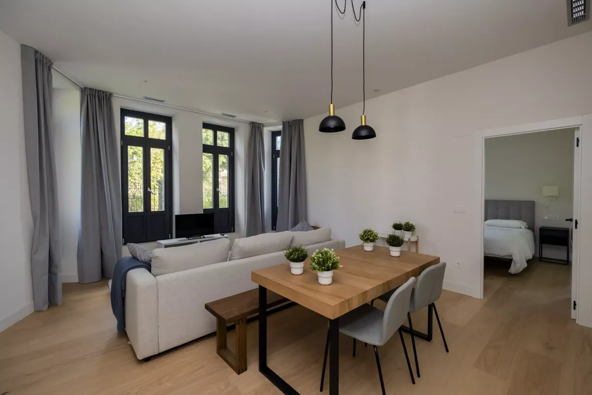 Mesa con silla y banca, macetas sobre la mesa de decoración, sofá y ventanal.