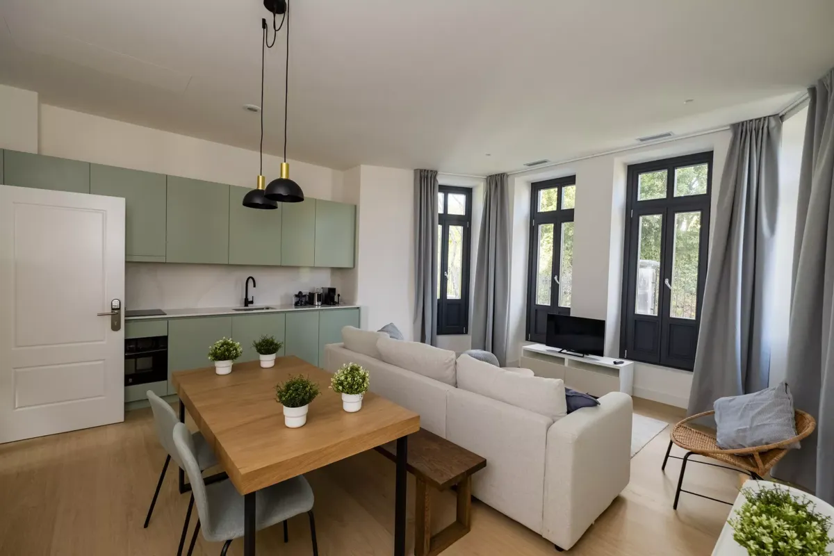 Mesa con silla y banca, 4 macetas sobre la mesa de decoración, sofá y ventanal.